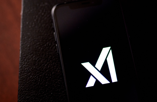 Um smartphone exibindo o logotipo branco 'xAI' em tela preta, parcialmente sobre uma superfície escura.