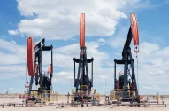 Três bombas de extração de petróleo em um terreno árido com céu azul e nuvens, destacando uma operação industrial.