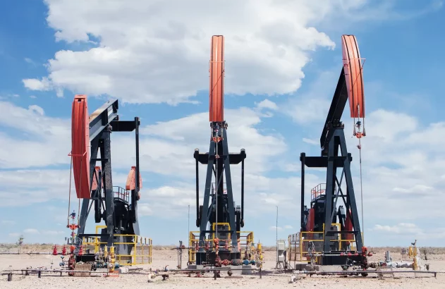Três bombas de extração de petróleo em um terreno árido com céu azul e nuvens, destacando uma operação industrial.