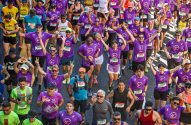 Multidão de corredores com camisetas roxas sorrindo e acenando em uma corrida de rua, a 99ª São Silvestre.