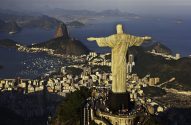 Vista aérea do Cristo Redentor no Rio de Janeiro, com a cidade e o Pão de Açúcar ao fundo.
