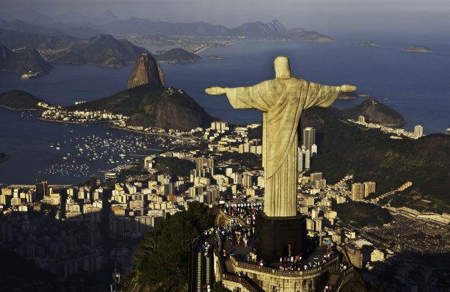 Vista aérea do Cristo Redentor no Rio de Janeiro, com a cidade e o Pão de Açúcar ao fundo.