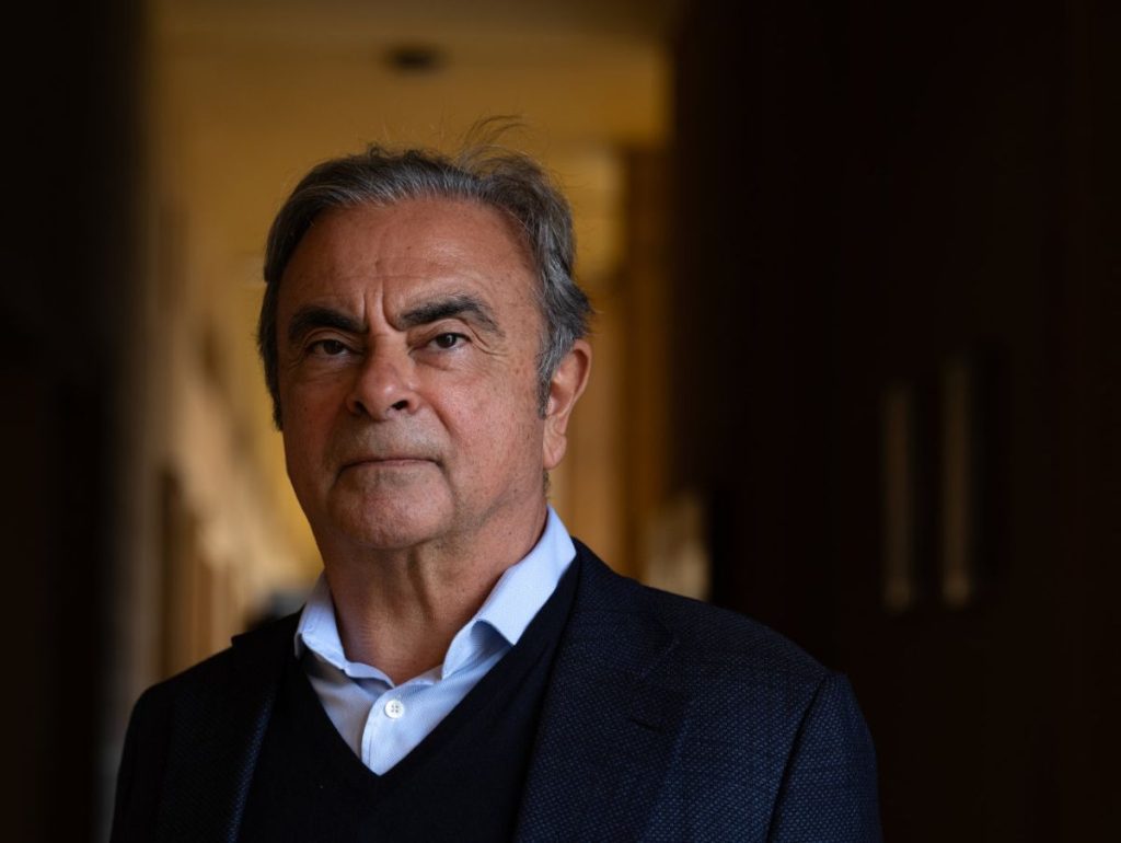 Carlos Ghosn foi CEO da Nissan, é um homem de cerca de 70 anos, está com uma blusa preta e uma camisa azul