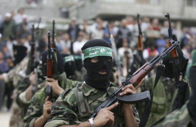 Grupo de homens de balaclava preta e uniformes camuflados, empunhando fuzis. Um usa faixa verde na cabeça.