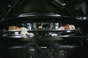 Dois homens inspecionam componentes dentro de um carro preto da Hyundai.