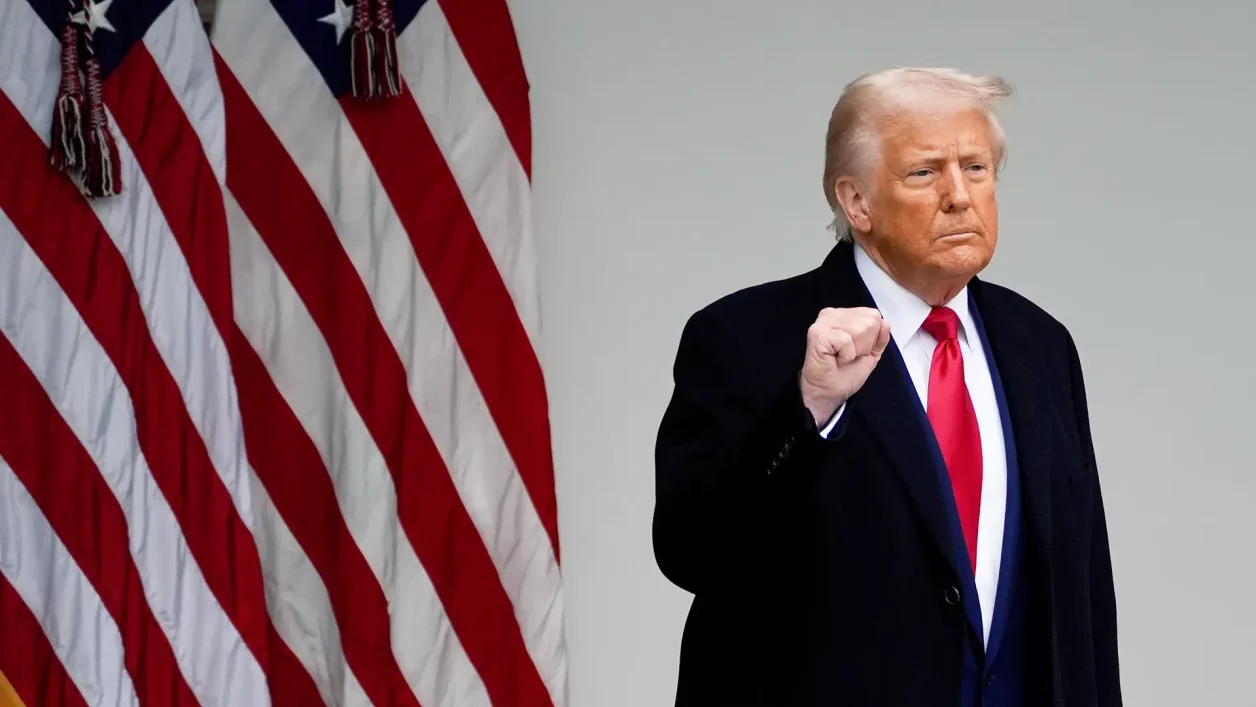 Donald Trump, punho cerrado, de casaco escuro e gravata vermelha, com bandeiras americanas ao lado.