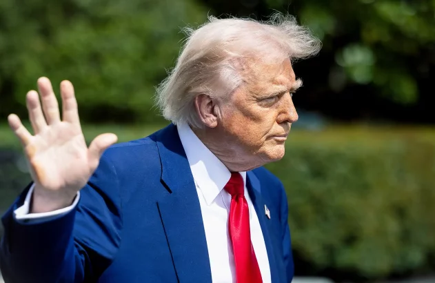 Donald Trump, de perfil, com terno azul, gravata vermelha e mão levantada em gesto de parada.