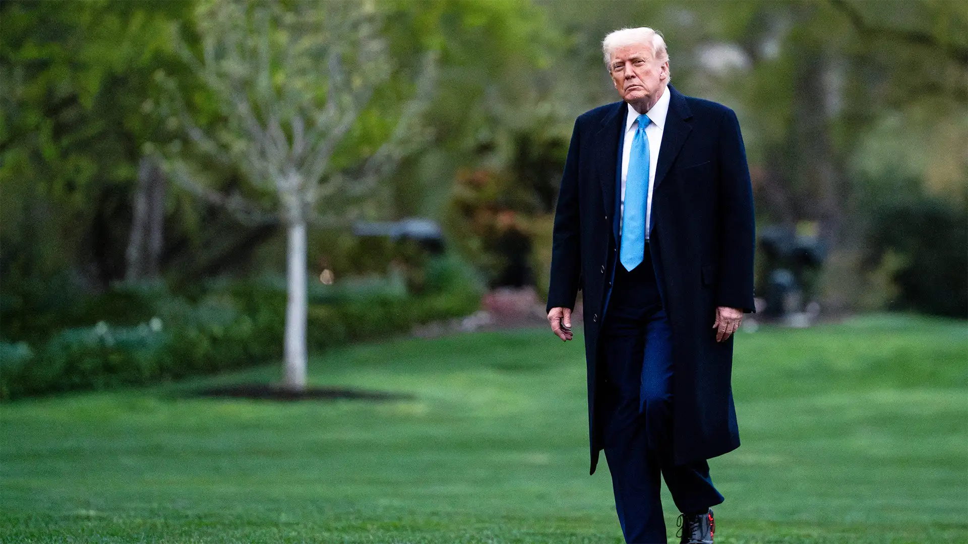 Trump está de terno preto e gravata azul e caminha para falar com jornalistas sobre as tarifas