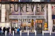 Fachada de loja Forever 21 com portas e vitrine de vidro. Cartazes indicam liquidação e encerramento de loja.