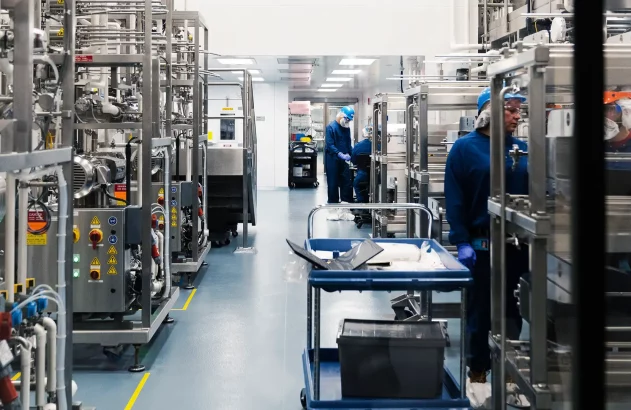 Pessoas com EPIs azuis operam maquinário de aço inox em uma instalação industrial limpa e moderna.