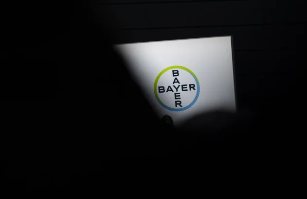 Mão segura tela iluminada exibindo o logo da Bayer, no escuro.