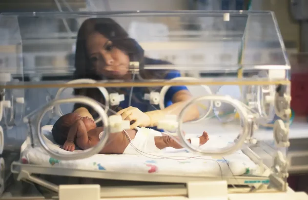 Enfermeira cuida de recém-nascido em incubadora de UTI neonatal.