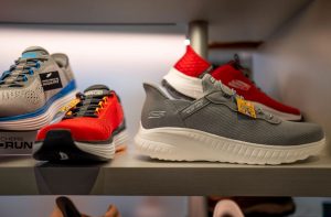 Tênis Skechers cinza, vermelho e azul expostos em prateleiras, destacando modelos GORUN, Wide Fit e Slip-ins.