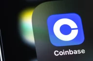 Imagem de um ícone azul com um "C" branco no centro, representando o aplicativo Coinbase. O nome "Coinbase" aparece em letras brancas abaixo do ícone, com fundo desfocado em tons de verde e amarelo.