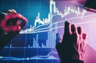 Imagem de duas mãos interagindo com uma tela eletrônica exibindo gráfico financeiro com linhas e barras nas cores branca e azul.
