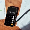 Ambiente de escritório com mesa de madeira, documentos e smartphone. Smartphone mostra tela de calculadora com número 12.568, cercado por papéis, gráficos coloridos e caneta preta.