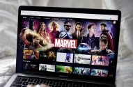MacBook Pro com Disney+ aberto na página da Marvel, mostrando super-heróis e títulos de filmes e séries.