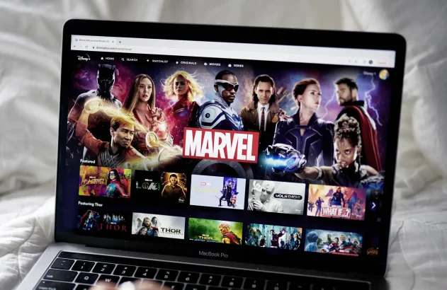 MacBook Pro com Disney+ aberto na página da Marvel, mostrando super-heróis e títulos de filmes e séries.