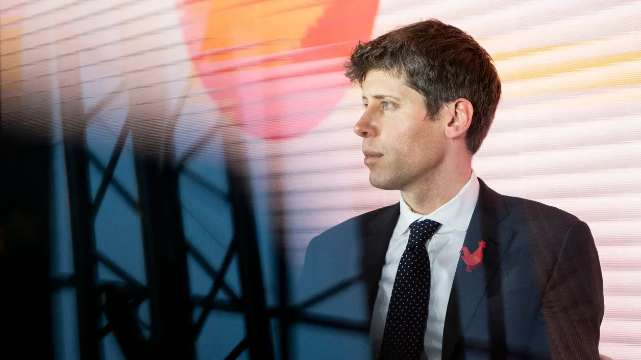 Sam Altman, CEO da OpenAI, de perfil com terno escuro, camisa branca e gravata preta com bolinhas brancas, broche de galo vermelho. Fundo listrado em laranja, amarelo e branco, com círculo laranja, e silhueta de estrutura metálica à frente.