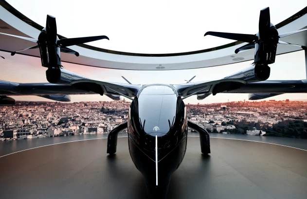 eVTOL preto em plataforma, com cidade ao entardecer no fundo.