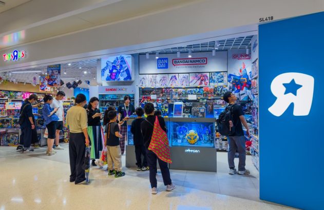 Pessoas exploram brinquedos e kits na entrada de uma loja Toys 'R' Us com espaço Bandai Namco/Gunpla.