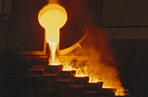 Metal fundido é vazado de uma concha em moldes escalonados, em processo industrial.