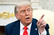 Donald Trump está com terno escuro e gravata vermelha, e aponta para à esquerda