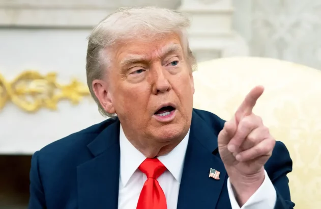 Donald Trump está com terno escuro e gravata vermelha, e aponta para à esquerda