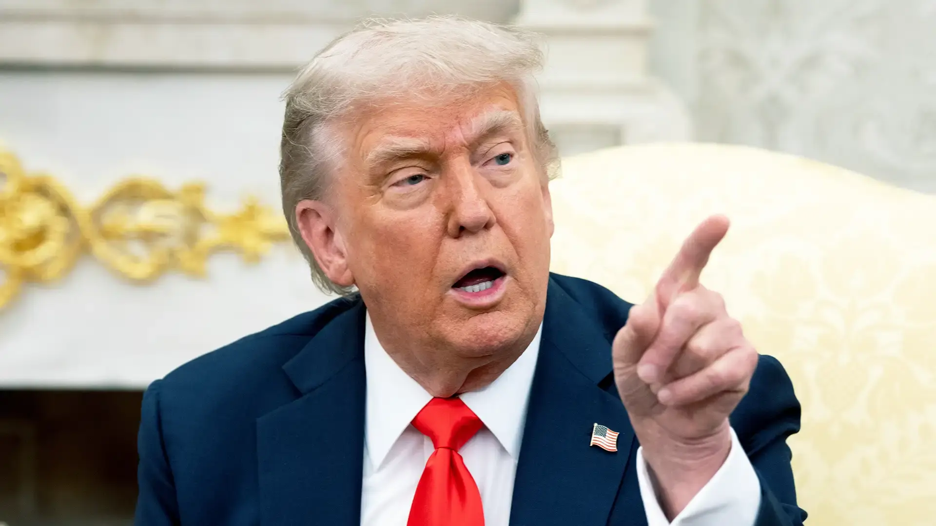 Donald Trump está com terno escuro e gravata vermelha, e aponta para à esquerda
