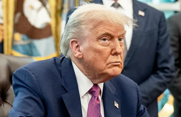 Trump está de terno azul e gravata roxa, olhando de lado, com cara de enfezado