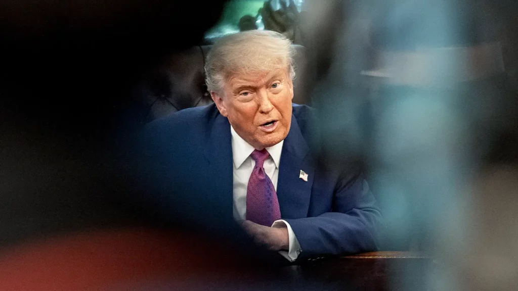 Donald Trump está com um terno azul, gravata roxa, olhando feroz para o lado direito da câmera
