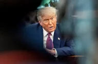 Donald Trump está com um terno azul, gravata roxa, olhando feroz para o lado direito da câmera