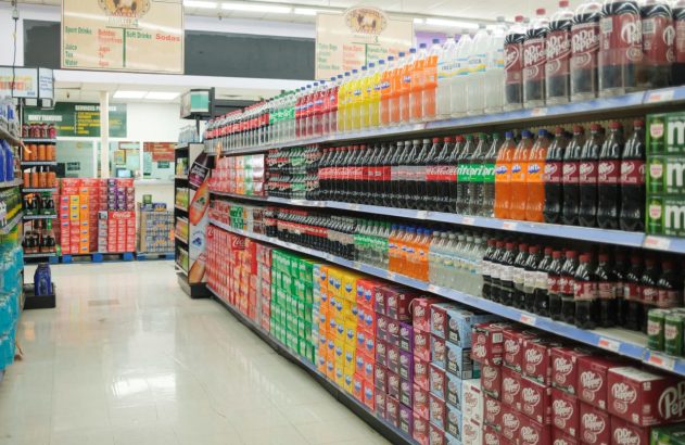 Corredor de supermercado com prateleiras cheias de bebidas em garrafas e caixas.