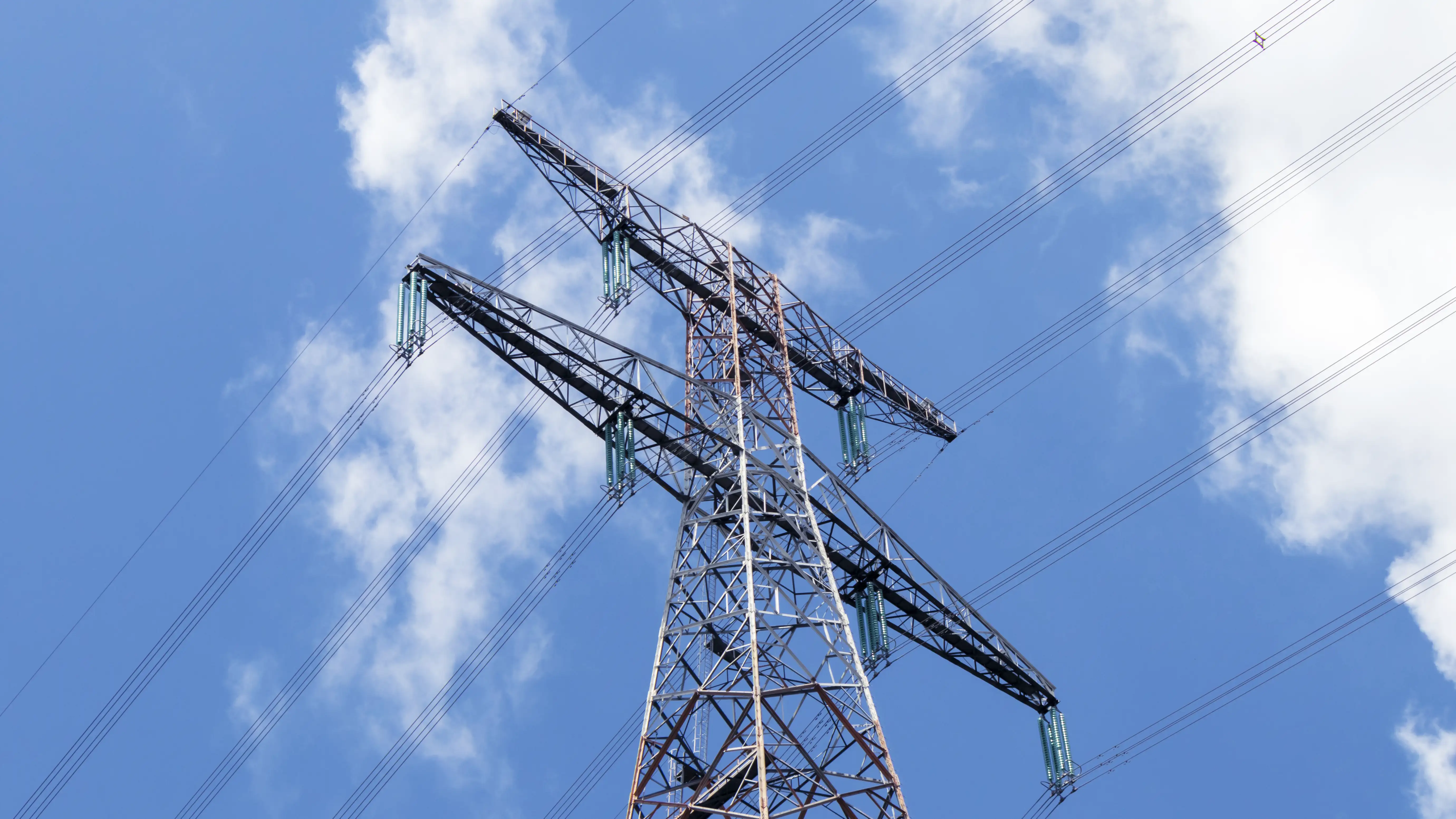 Topo de uma torre de transmissão de energia elétrica contra um céu azul