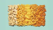 Variedade de salgadinhos organizados em faixas sobre fundo azul claro. Sequência de wafers claros, salgadinhos espiralados laranja, batatas fritas onduladas amarelas, nachos triangulares alaranjados e biscoitos quadrados laranja tostados.