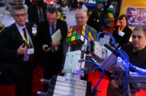 Imagem de uma mão de robô montando um cubo mágico e pessoas olhando a cena