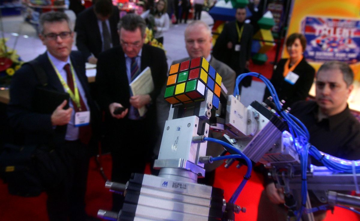 Imagem de uma mão de robô montando um cubo mágico e pessoas olhando a cena