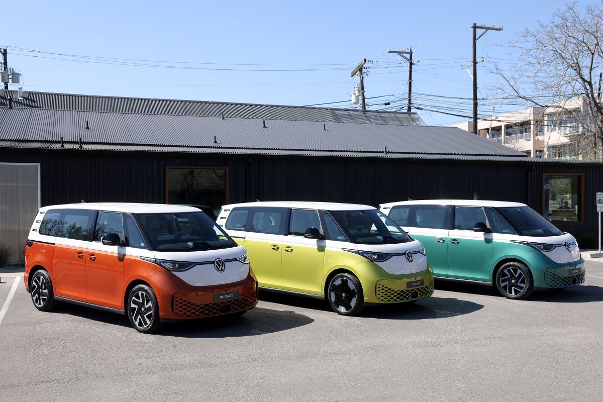 Três Kombis elétricas da Volkswagen, com a frente mais quadrada, uma é vermelha, outra amarela e a terceira, verde