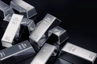 A imagem mostra várias barras de prata polidas sobre uma superfície escura, exibindo brilho sob a luz. Cada barra é marcada com "FINE SILVER 999.9" e "NET WT 1000 g", indicando prata pura de 1000 gramas, organizadas aleatoriamente com leves sobreposições.