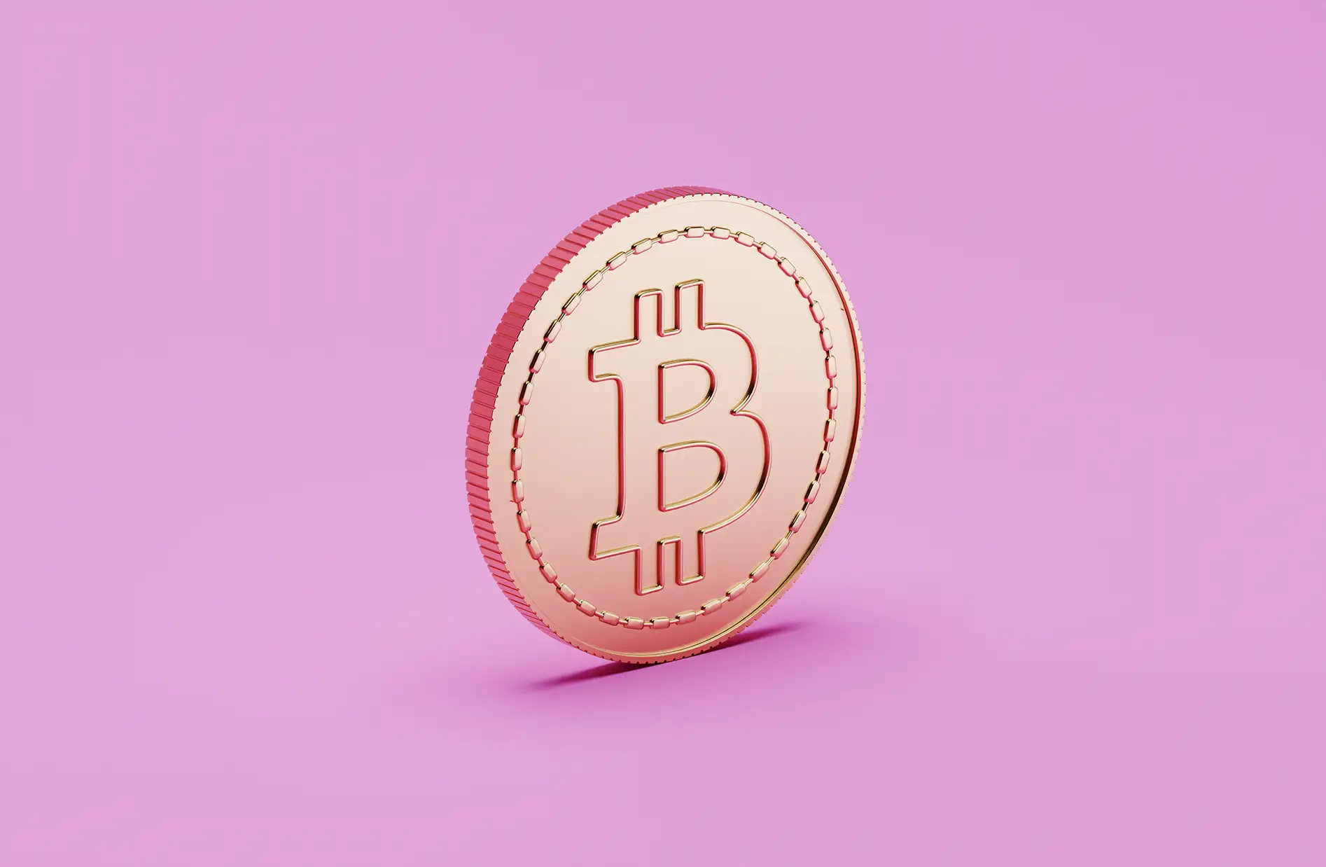 A imagem apresenta uma moeda com o símbolo do Bitcoin em destaque, posicionada sobre um fundo rosa sólido. A moeda possui um brilho metálico característico, com entalhes na borda e sombra ao fundo, enfatizando seu relevo e detalhes.