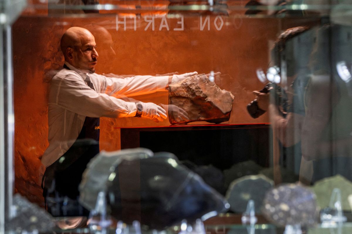 Imagem mostra um homem careca segurando uma grande pedra, que é meteriorito de Marte