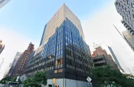 Prédio da Arquidiocese de Nova York visto de baixo para cima: préido alto, metade de cima bate sol, metade debaixo está na sombra, todo em tom escuro, sob céu azul, bem na esquina