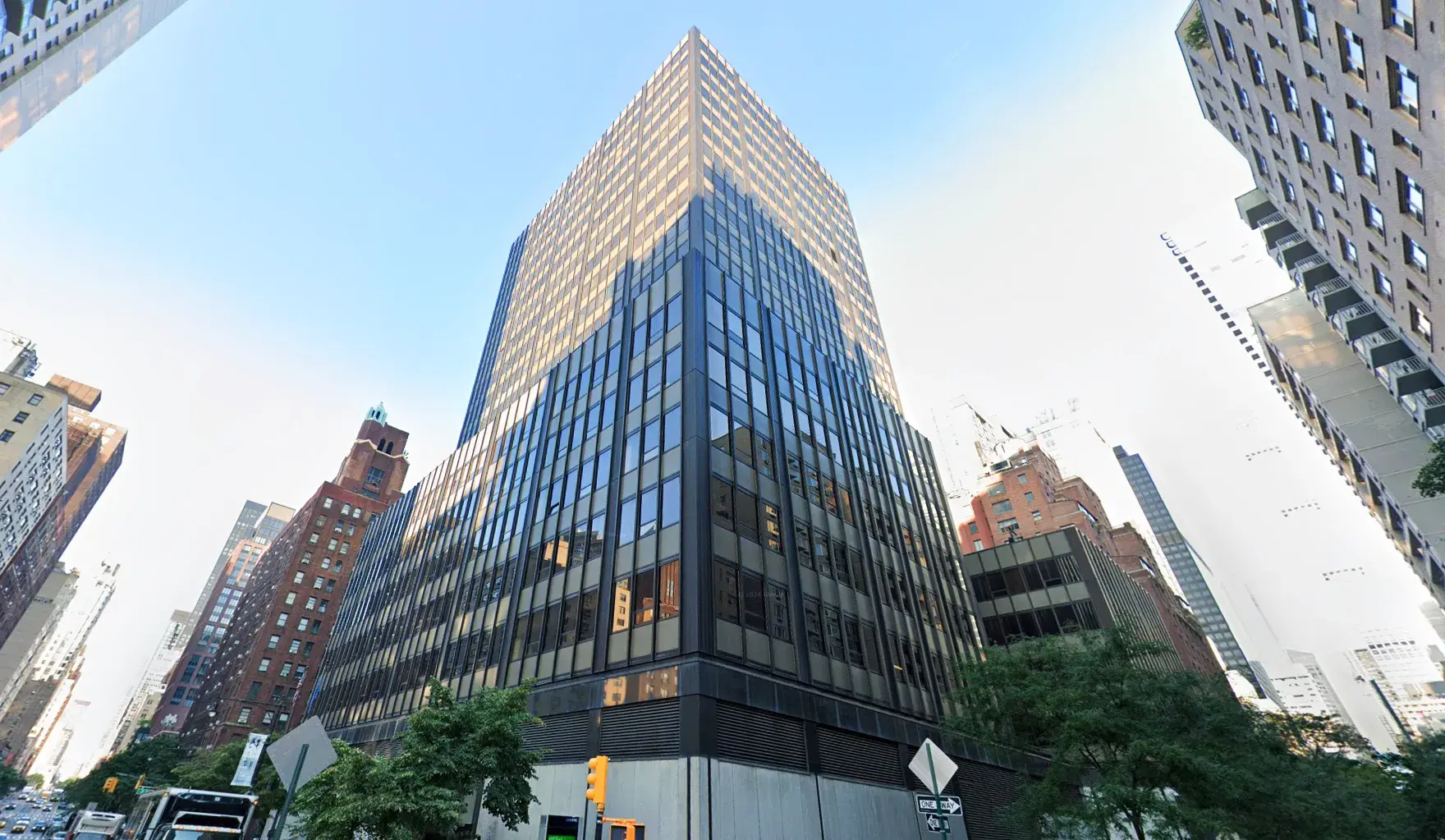 Prédio da Arquidiocese de Nova York visto de baixo para cima: préido alto, metade de cima bate sol, metade debaixo está na sombra, todo em tom escuro, sob céu azul, bem na esquina
