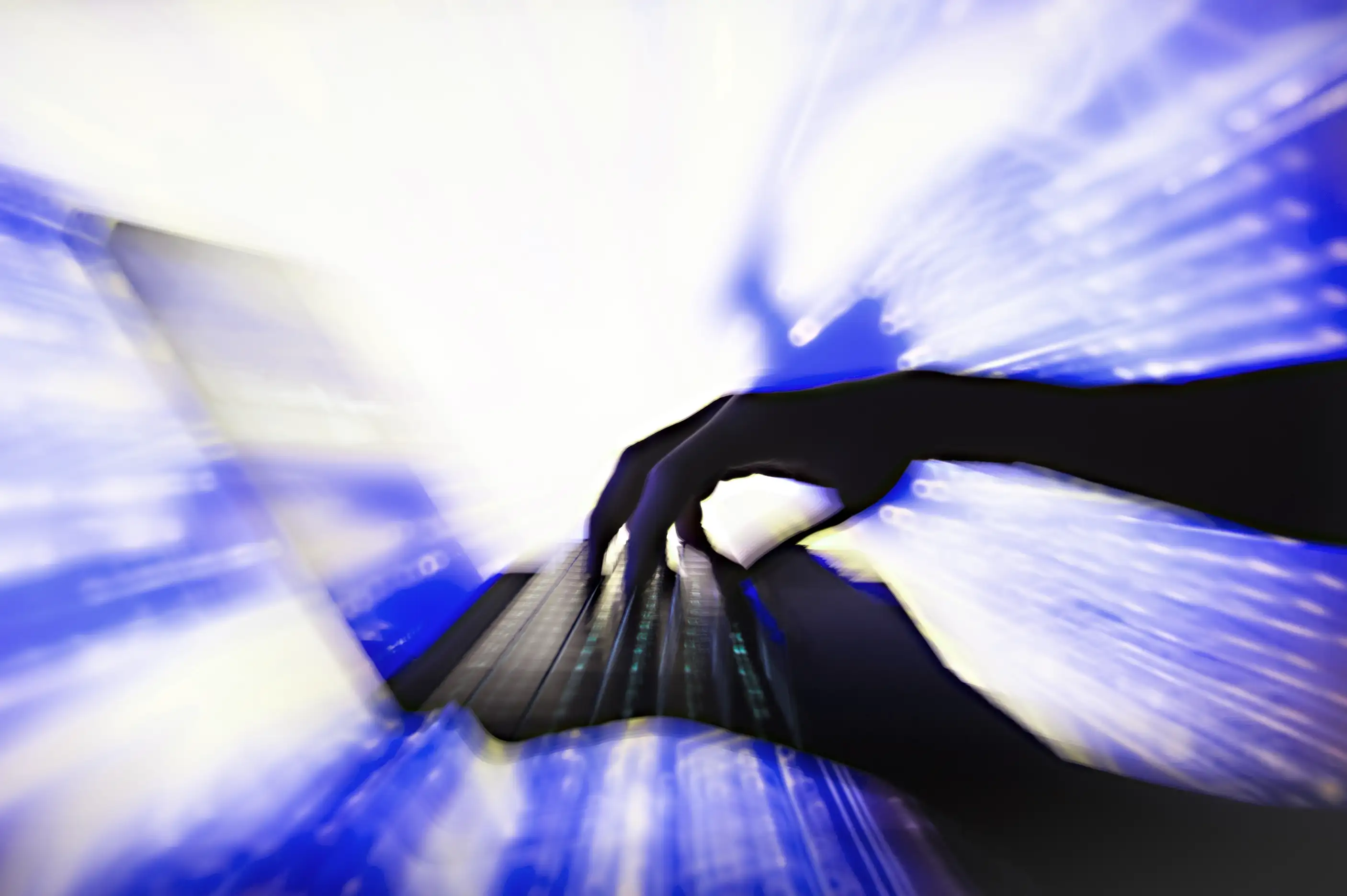 A imagem mostra uma mão em silhueta sobre um teclado de computador preto com iluminação sob as teclas. O fundo, desfocado em azul e branco, cria uma sensação de movimento e dinamismo, sugerindo rapidez na digitação ou interatividade digital, com padrões de luz evocando energia ou fluxo de dados.