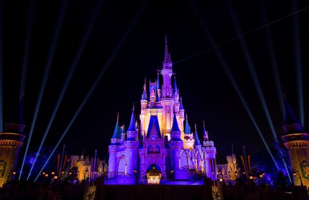 Imagem mostra o Castelo da Cinderela, na Disney, em uma noite. Castelo está iluminado com luz roxa