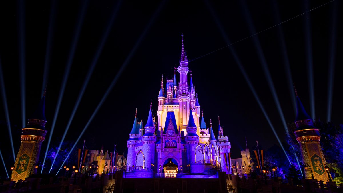 Imagem mostra o Castelo da Cinderela, na Disney, em uma noite. Castelo está iluminado com luz roxa