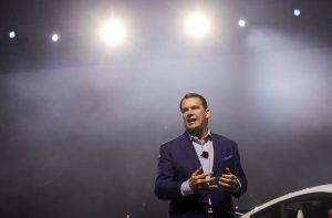 CEO da Ford, Jim Farley, está de paletó preto dando uma palestra