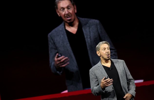 Fundador da Oracle está de paletó cinza e camiseta preta dando uma palestra