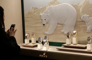 Vitrine onde estão seis relógios Rolex e uma mulher do lado de fora fotografando