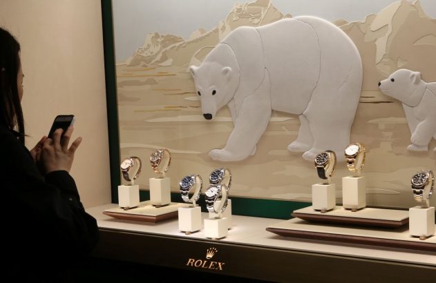 Vitrine onde estão seis relógios Rolex e uma mulher do lado de fora fotografando